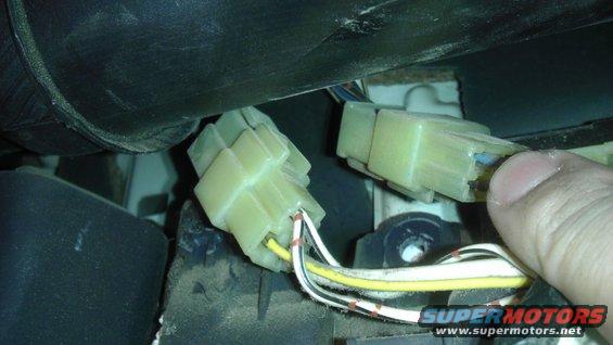 Close-up of two yellow electrical connectors with wires, one being held by a thumb