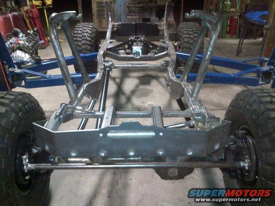 Jeep CJ frame, suspension, and tires in a workshop. The frame appears to be modified or under construction