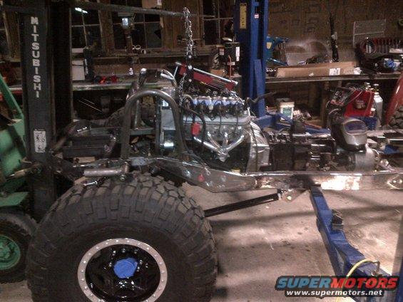 Jeep CJ frame on lift with engine being installed. Forklift in background