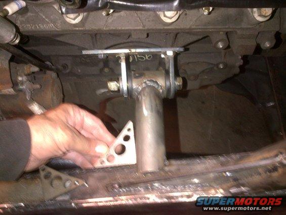 Undercarriage of a vehicle with a hand holding a metal bracket near a welded pipe and engine block
