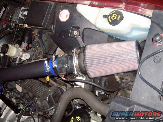 Close-up of an aftermarket air intake with a cone filter and mass airflow sensor on an engine