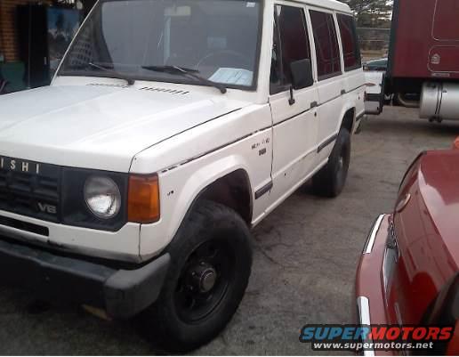 White Mitsubishi Montero SUV parked next to a red car and a semi-truck