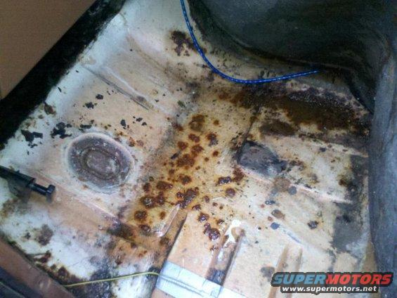 Vehicle floor pan with rust and dirt, showing some wiring and a bolt
