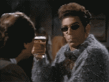 Man in sunglasses and a fuzzy sweater raises a glass of beer
