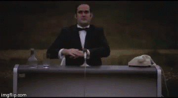 Man in tuxedo behind desk with rotary phone and liquor bottle