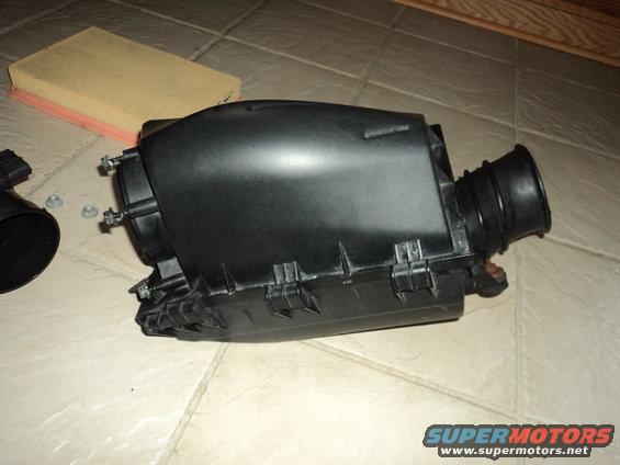 Black plastic air filter housing with intake hose and air filter on tiled floor