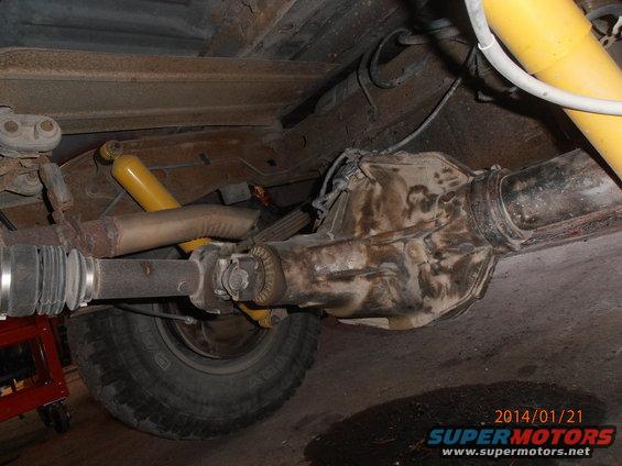 Underside view of a vehicle's rear axle, driveshaft, and yellow shock absorber