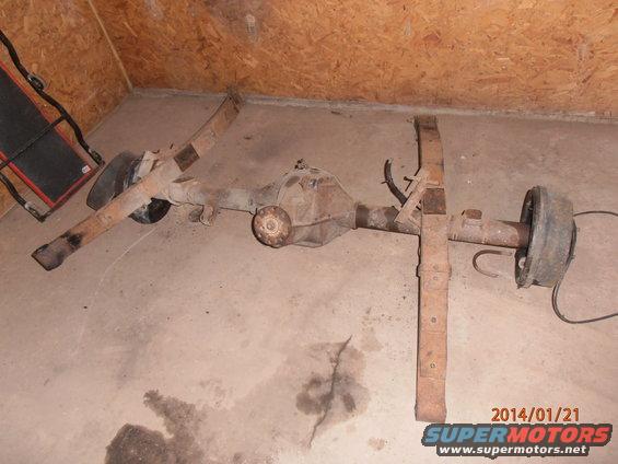 Rear axle assembly with leaf springs and brake drum, rusty, on concrete floor