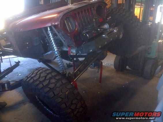 Red Jeep CJ-series front end with large tires and suspension visible, being worked on