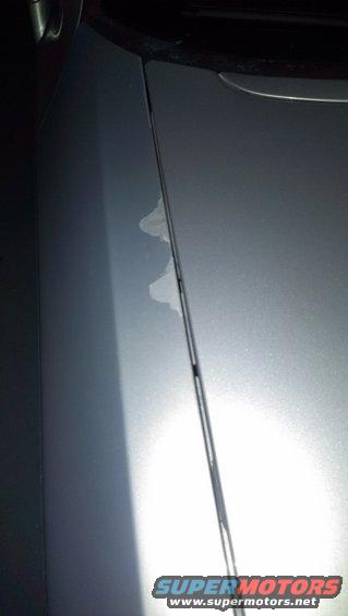 Silver car door seam with peeling paint and a Supermotors.net watermark