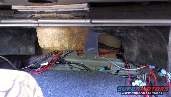 Car trunk interior with exposed wiring, a subwoofer enclosure, and insulation material