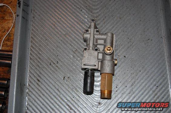 Metal valve assembly with brass fitting and black plastic component on a ribbed metal surface