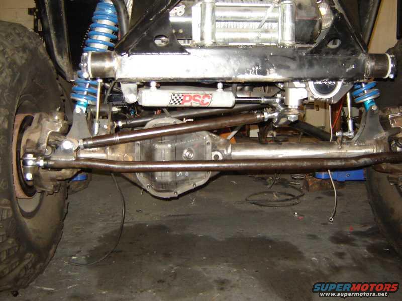 close-up of off-road vehicle's front axle, steering linkage, and blue shocks