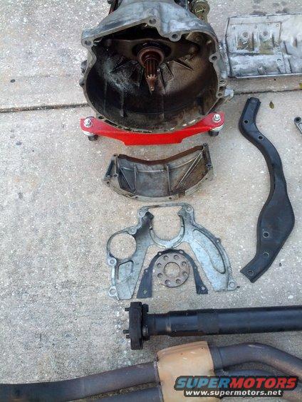 Transmission bell housing, driveshaft, and exhaust components laid out on concrete