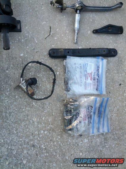 Car parts including a driveshaft, sensor, shifter linkage, and bagged hardware on concrete