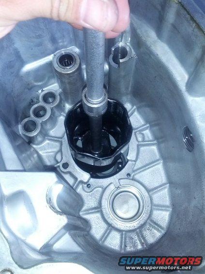 Using a tool to remove a black part from inside a metal transmission housing