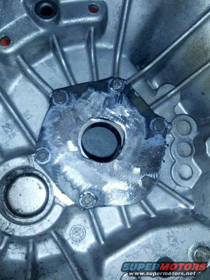Close-up of a metal part with a hole in the center, bolted onto a larger housing. Some weld marks are visible