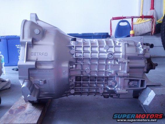 Silver Getrag 260 transmission on wooden blocks, with blue recycling bin and cleaning supplies in background