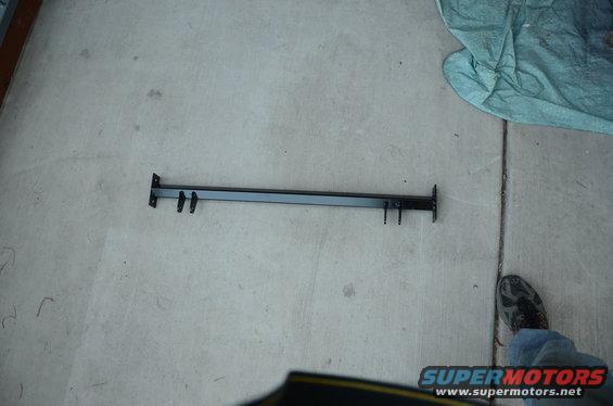 Black metal bar with four prongs, lying on concrete