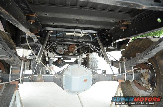 Underside view of a lifted 4x4 truck showing the rear axle, leaf springs, transfer case, and exhaust system