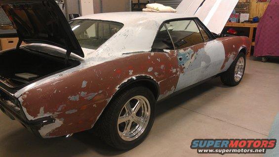 car body in primer and rust, hoods open, in a garage