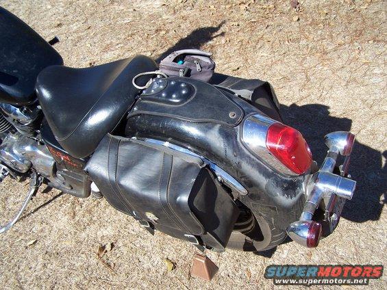 Close-up of a motorcycle's rear fender, taillight, and leather saddlebags. A small bag is on the seat