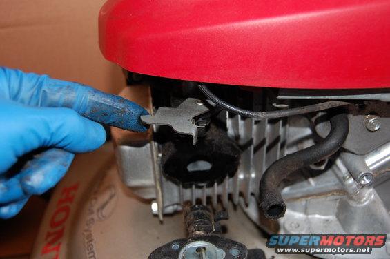 Gloved hand adjusting a linkage on a Honda engine. Part of a red cover is visible