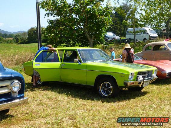 Lime green sedan with open driver's door, parked on grass next to a blue truck