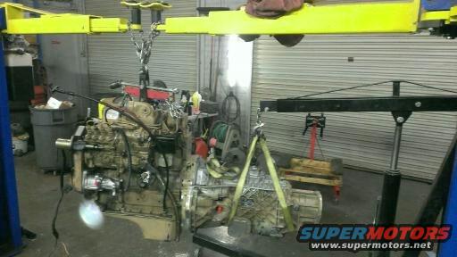 Engine and transmission assembly suspended by a yellow engine hoist in a garage