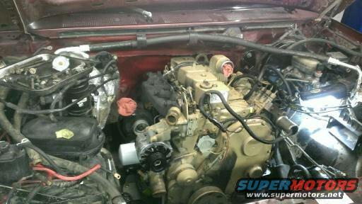 Engine bay with a large diesel engine, hoses, and wiring. Red vehicle exterior visible