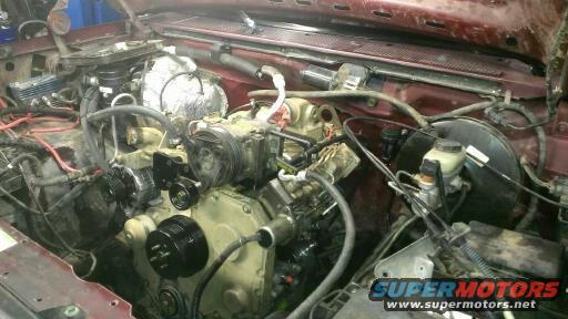 Engine bay with various components, hoses, and wiring visible. Supermotors.net logo in lower right