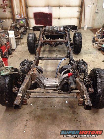 Vehicle frame, suspension, and wheels in a garage. Some parts are rusty