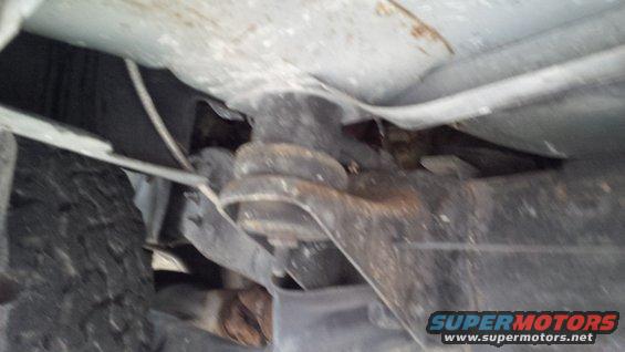Undercarriage of a vehicle showing suspension components and a tire. The metal parts are rusty