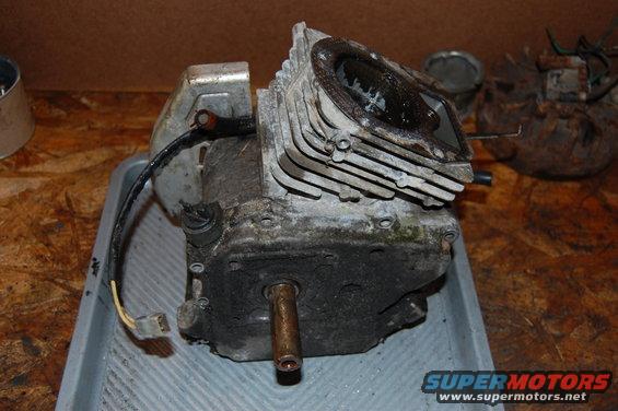 Dirty engine block with cooling fins and a metal shaft protruding from the bottom, resting in a gray tray