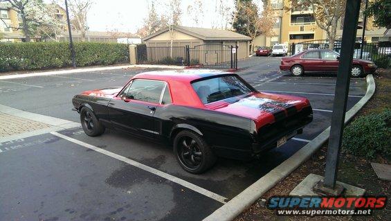 Black 1967 Ford Mustang with red roof and red stripe on trunk, parked in a lot