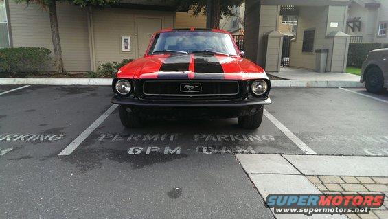 Red 1967 Ford Mustang with black racing stripes parked in a lot