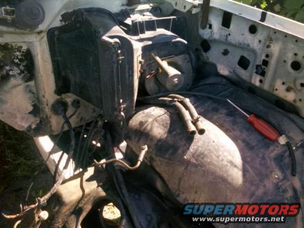 Engine bay with radiator, heater core, and large black component. Screwdriver rests on top