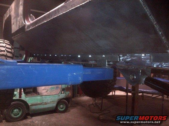 underside of vehicle frame with blue support beams and a forklift underneath