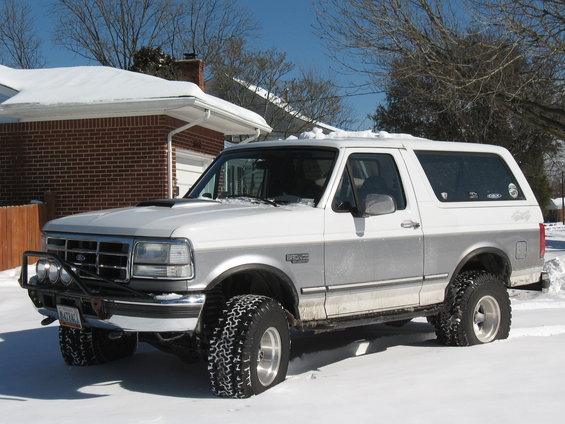 White and silver Ford Bronco with aftermarket bumper and lights parked in snow