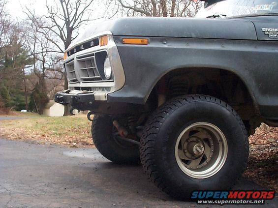 Front corner of a dark green Ford Bronco with a custom bumper. The grille and headlights are visible