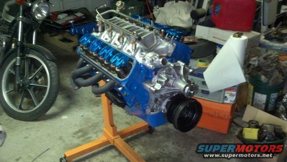 V8 engine on an orange stand, with a motorcycle to the left