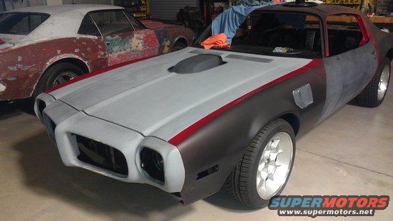 Unfinished 1970s Pontiac Firebird/Trans Am with primer and red stripe detail, seen from a 3/4 front angle