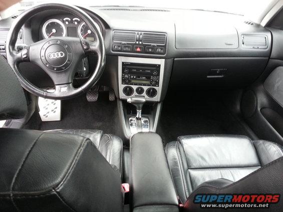 Interior shot of a car, showing the dashboard, steering wheel with Audi logo, center console with automatic shifter, and leather seats