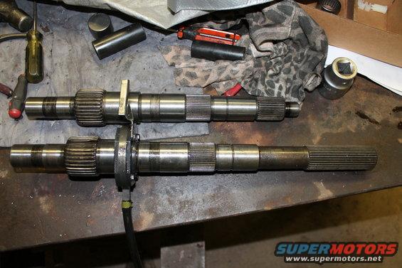 Two metal shafts with splines and gears sit on a workbench next to tools and rags