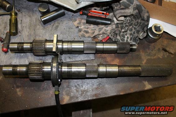 Two metal transfer case shafts with splines and gears on a workbench with tools