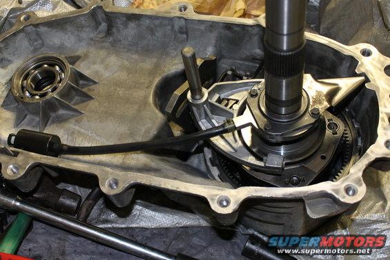 Transfer case interior with gears, shafts, and a bearing visible. A black cable is connected
