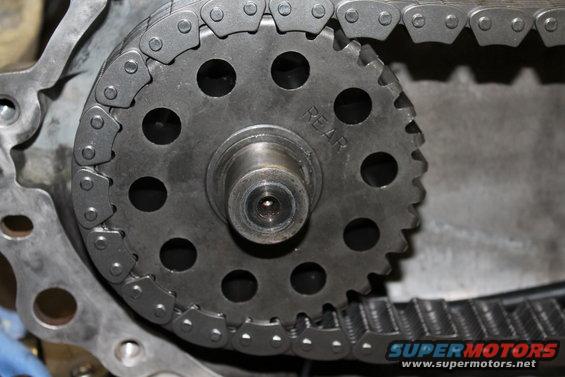 Close-up of a transfer case chain and gear with 'REAR' visible on the gear