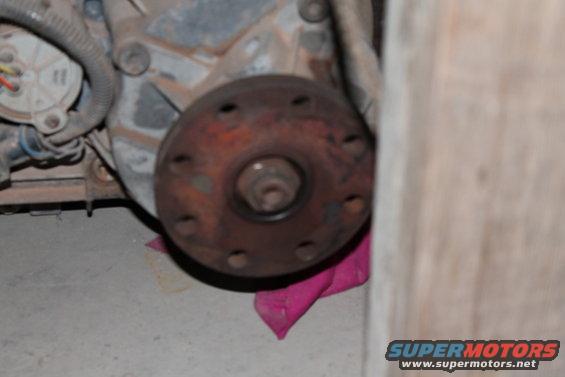 Rusty transfer case flange with bolt holes, attached to a gray metal housing. Pink cloth underneath