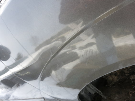 Close-up of a silver car fender with scratches and reflections