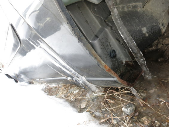 Underside of a dark-colored car with visible rust and ice on the rocker panel